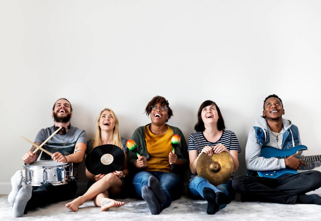 Cette image illustre l'article de Berwin Sydney qui parle de l’universalité de la musique Cinq jeunes adultes d’origines diverses rient et jouent de la musique ensemble avec des instruments variés, illustrant la diversité et l’universalité du langage musical.