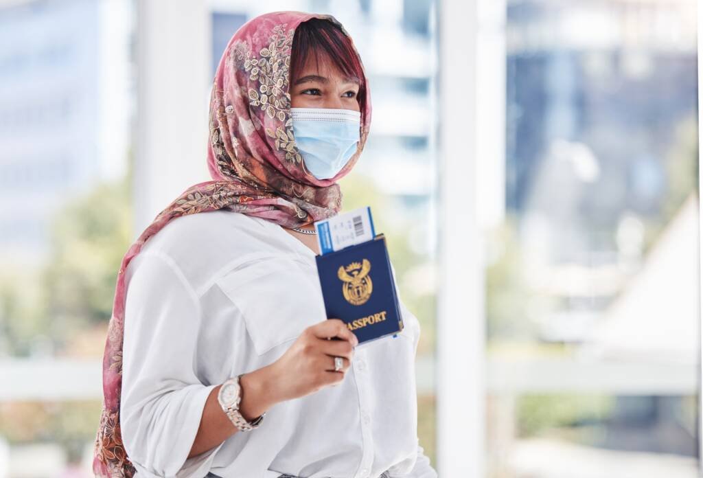 Femme immigrante portant un hijab et un masque, tenant un passeport et une carte d’embarquement à l’aéroport — symbole d’un nouveau départ et de la réinvention personnelle.