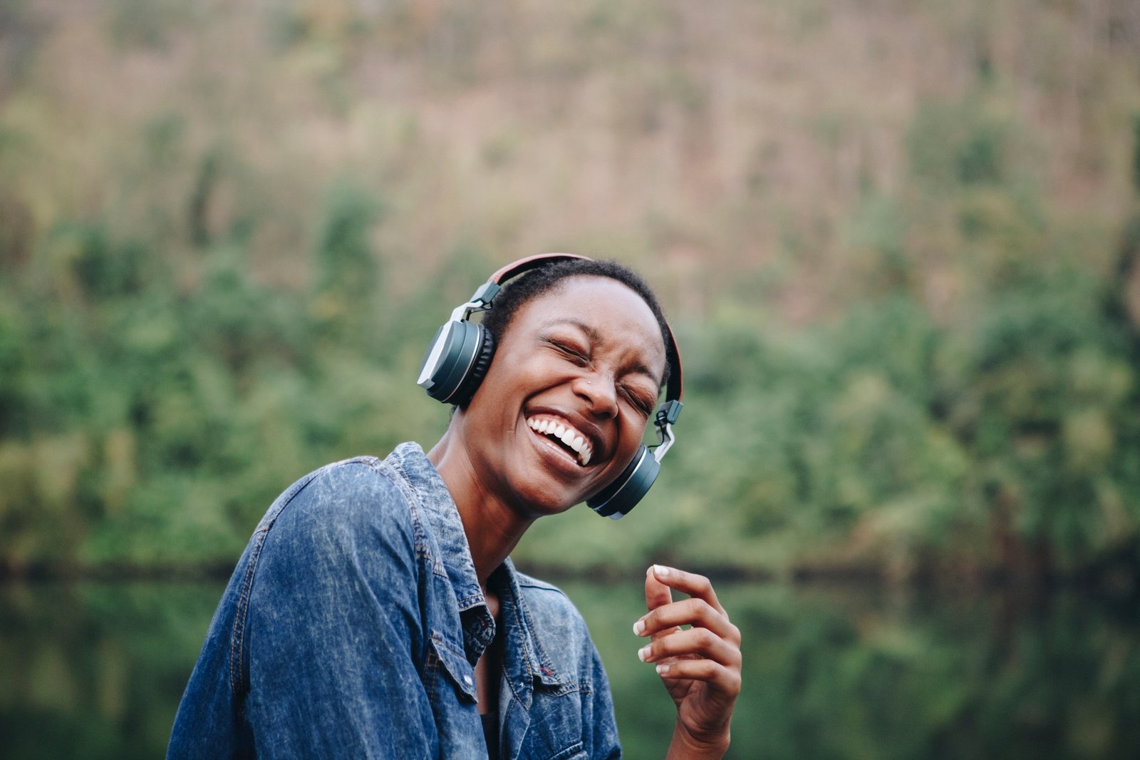 Femme noire souriante écoutant de la musique avec des écouteurs dans la nature, incarnant la puissance universelle de la musique.