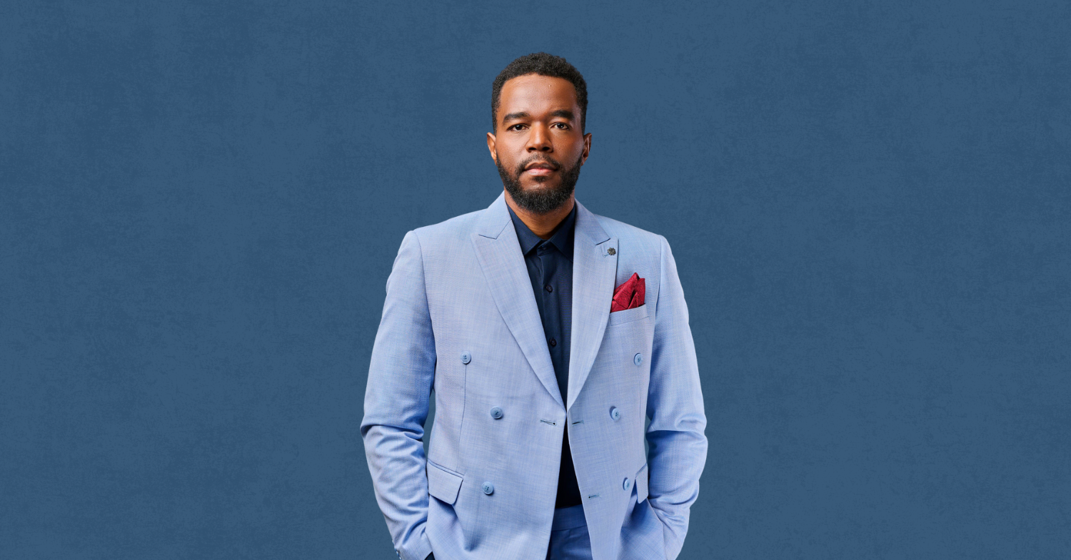 Portrait de Berwin Sydney Entrepreneur créatif et storyteller visuel à Ottawa, Berwin conçoit des images, récits et univers de marque pour leaders et institutions. Berwin en costume bleu clair, debout sur fond bleu texturé, regard droit et posture confiante, représentant son univers créatif et identitaire.