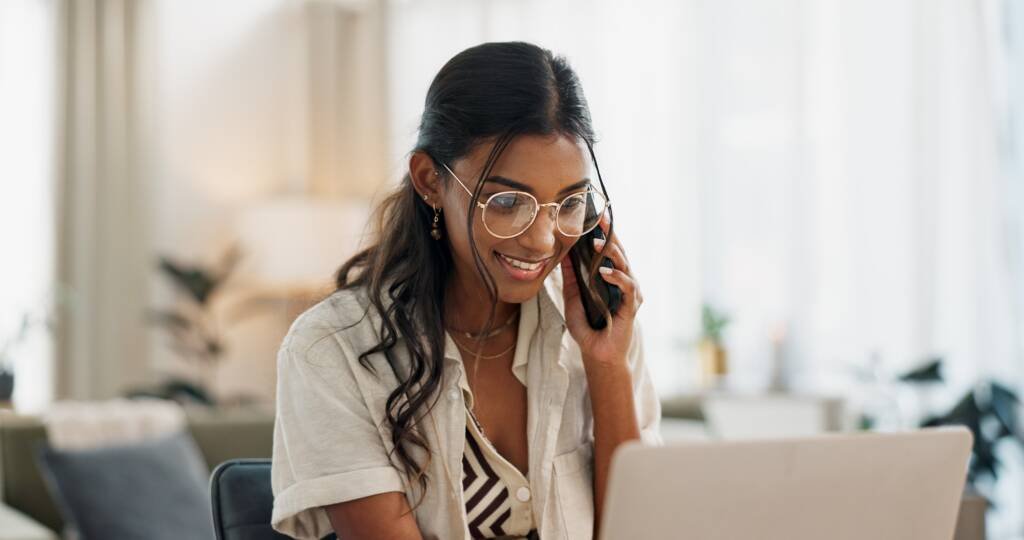 Jeune femme souriante au téléphone devant un ordinateur, travaillant sur la communication numérique d’un organisme à but non lucratif.