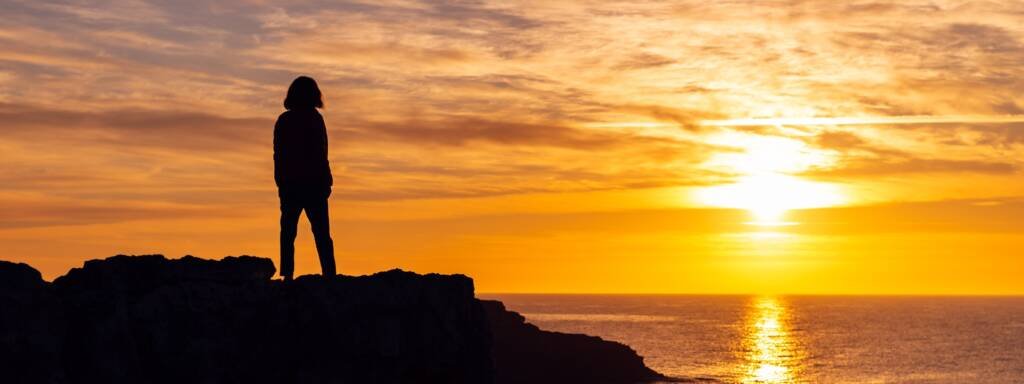 Silhouette d’une personne debout face à un lever de soleil sur l’océan, symbolisant l’espérance, la foi retrouvée et un nouveau départ.