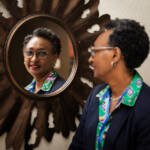 Portrait professionnel d’une femme élégante photographiée lors du symposium de la FCFA, capturée à travers un miroir décoratif en forme de soleil.