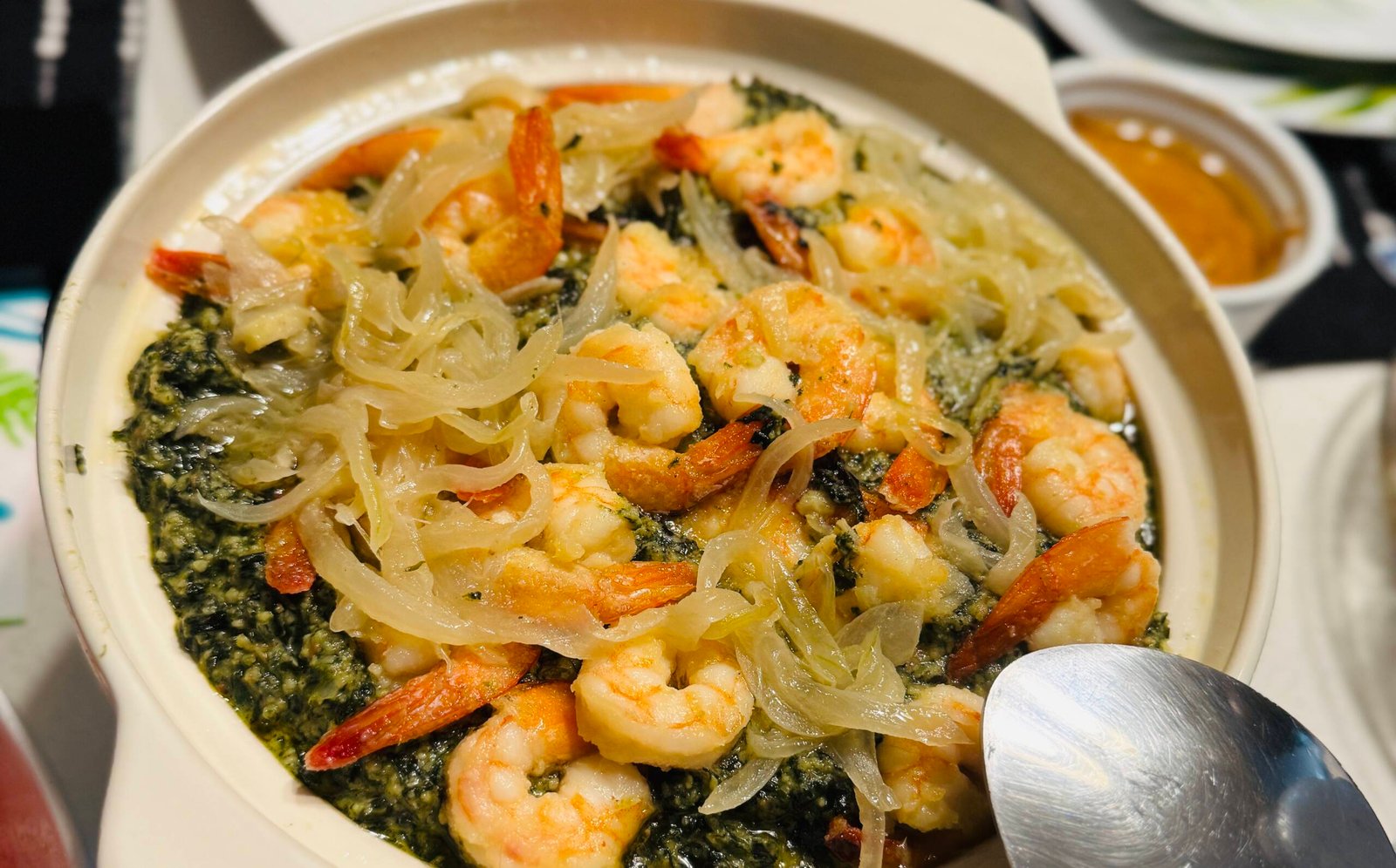 Plat traditionnel camerounais de Ndolè aux crevettes, servi avec oignons caramélisés, photographié en gros plan pour illustrer la richesse de la gastronomie d’Afrique centrale.