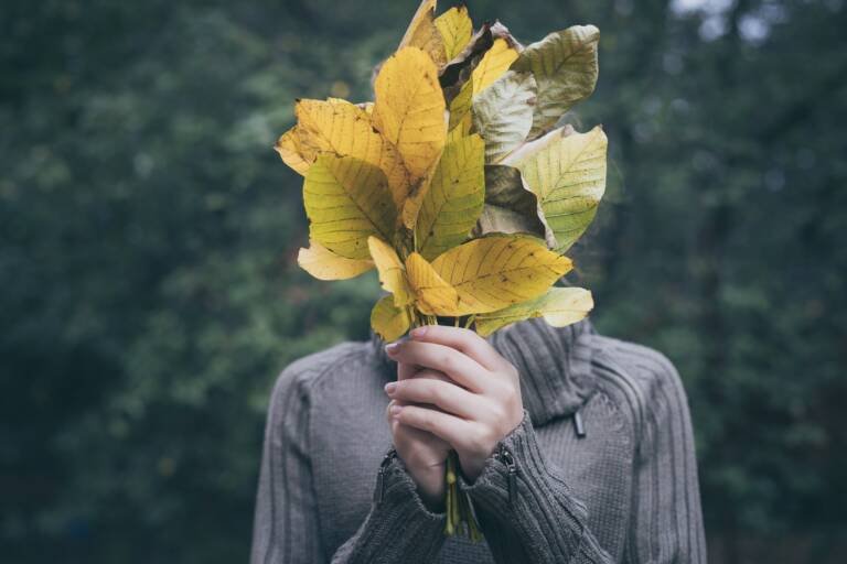 Personne cachant son visage derrière un bouquet de feuilles, symbole du syndrome de l’imposteur et du doute créatif.