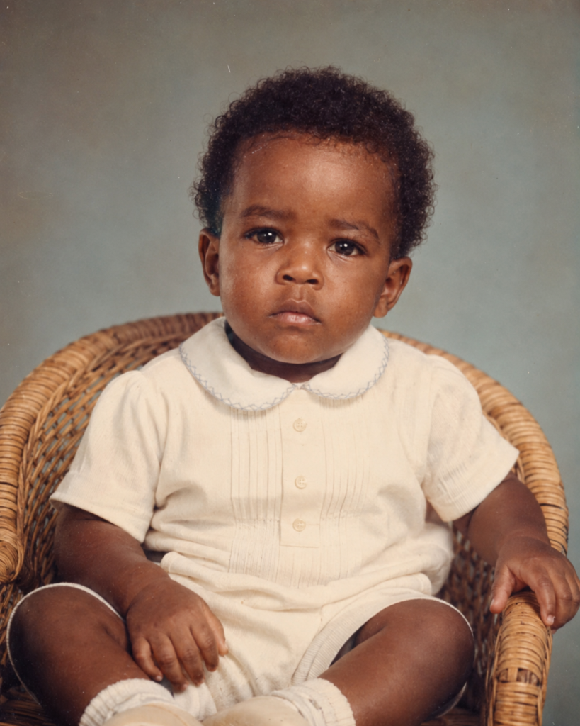 Berwin Sydney bébé, assis dans un fauteuil en osier, en barboteuse blanche