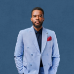 Berwin Sydney en complet bleu clair et pochette bordeaux, les mains dans les poches